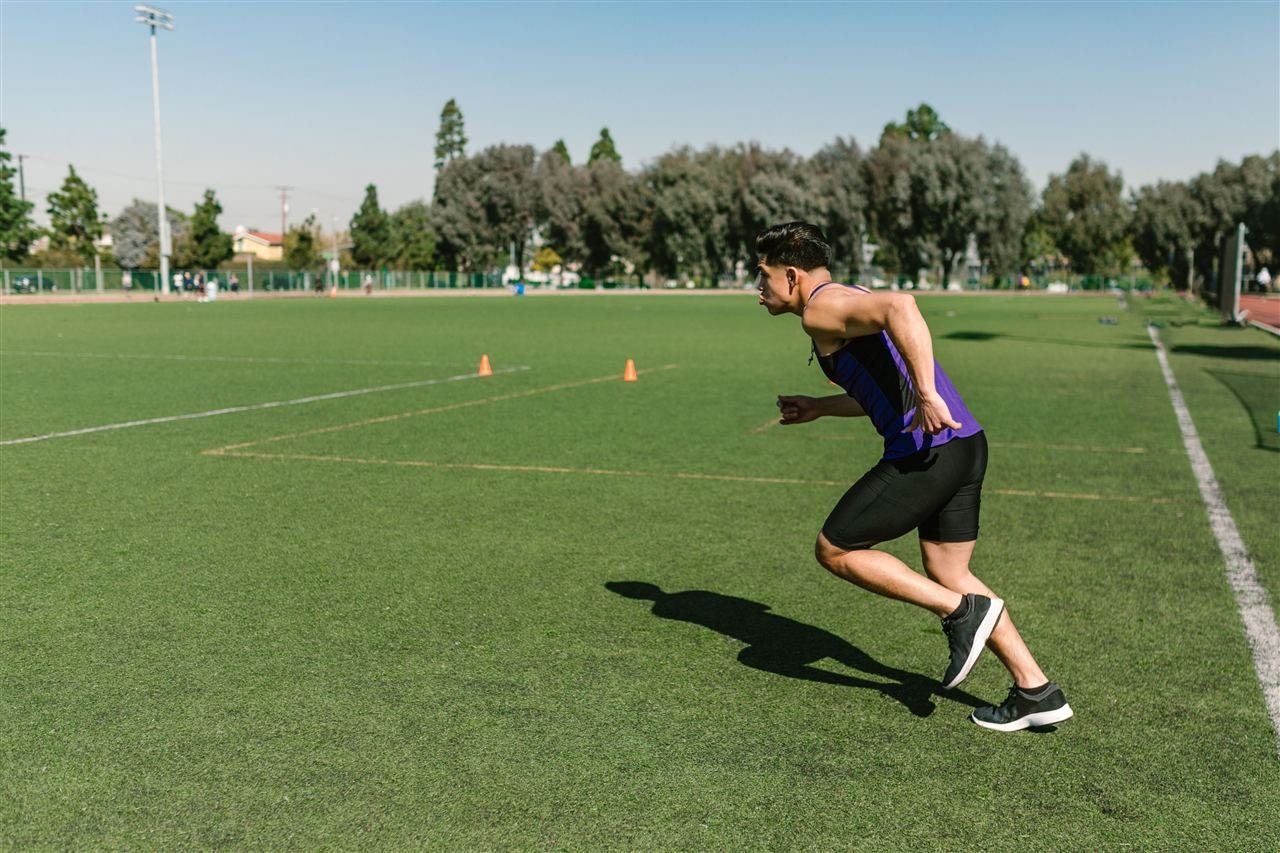 Atleta em pleno sprint durante treino intervalado, com cones de treino ao fundo
