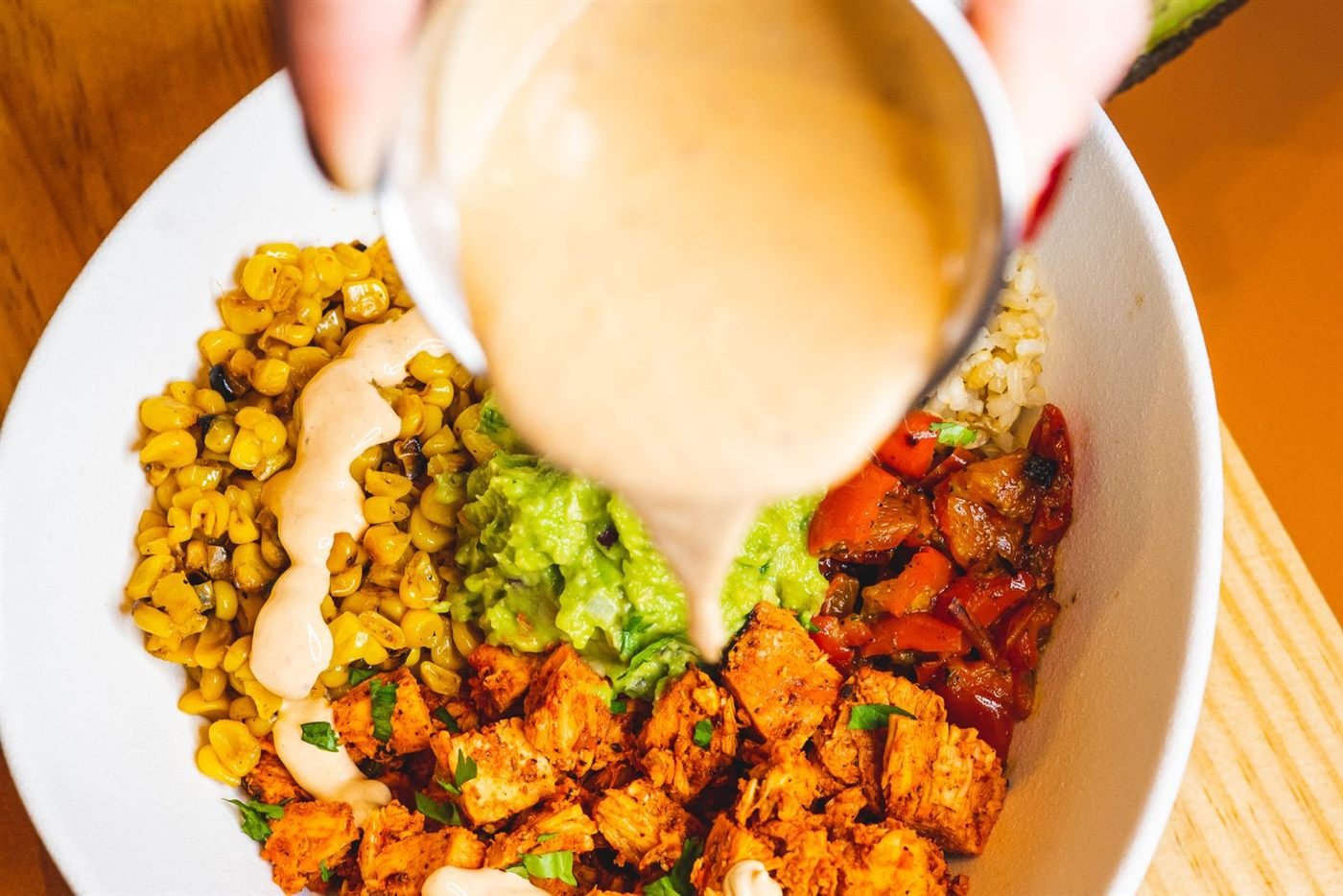 Bowl com frango temperado, milho, guacamole e molho sendo servido por cima