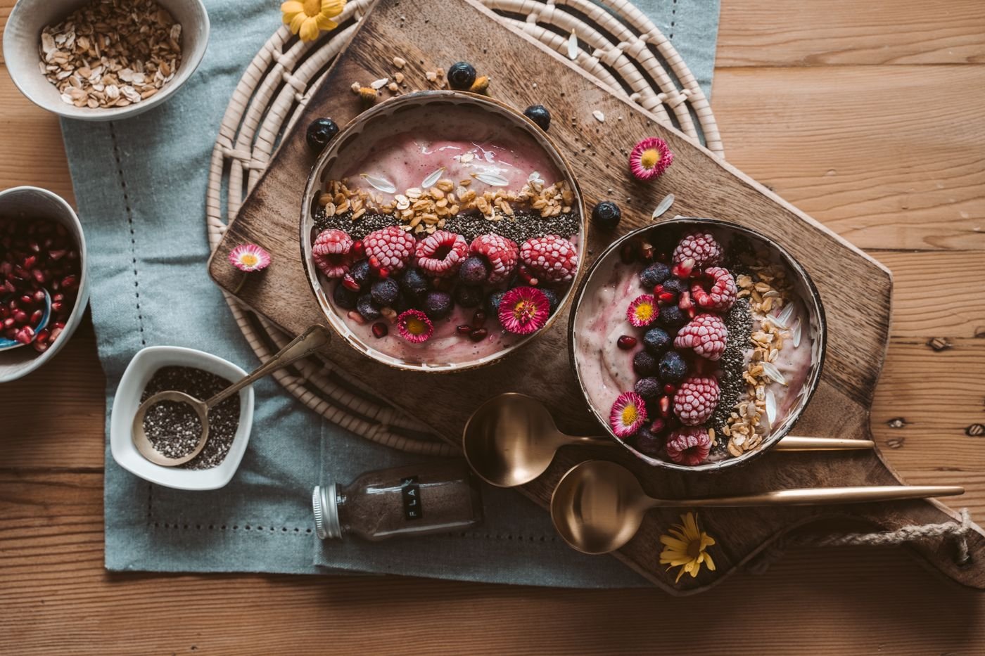 Bowls de smoothie de frutas vermelhas com granola vistos de cima sobre tábua de madeira