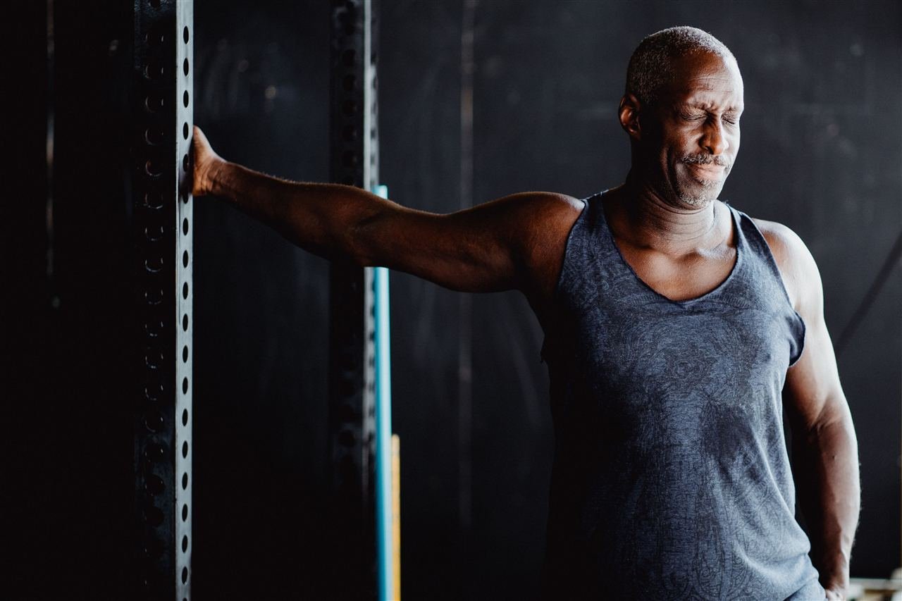 Homem de meia-idade se alongando antes de treino de musculação na academia