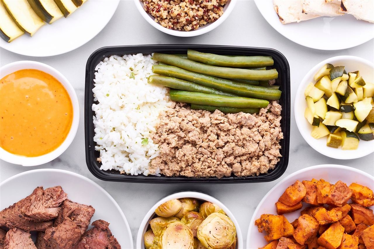 Marmitas de meal prep organizadas ao redor de uma refeição com arroz, frango e vegetais