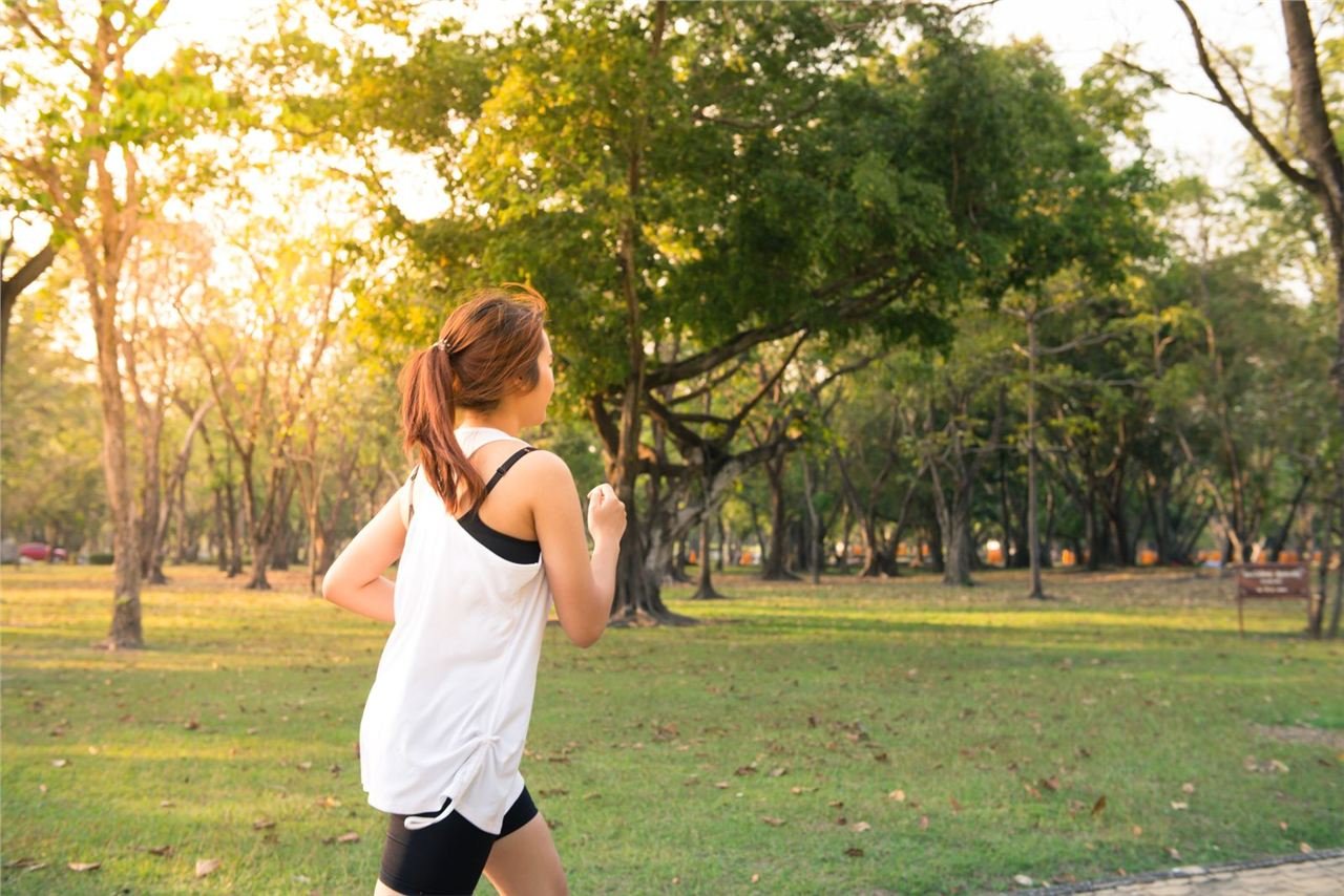 Mulher correndo em parque verde, vista de costas, treino cardiovascular