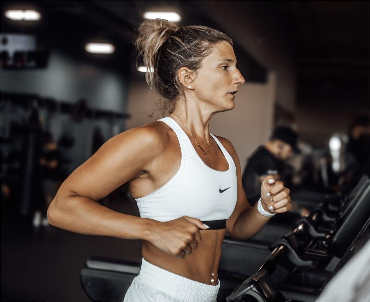 Mulher correndo em esteira durante treino cardiovascular na academia
