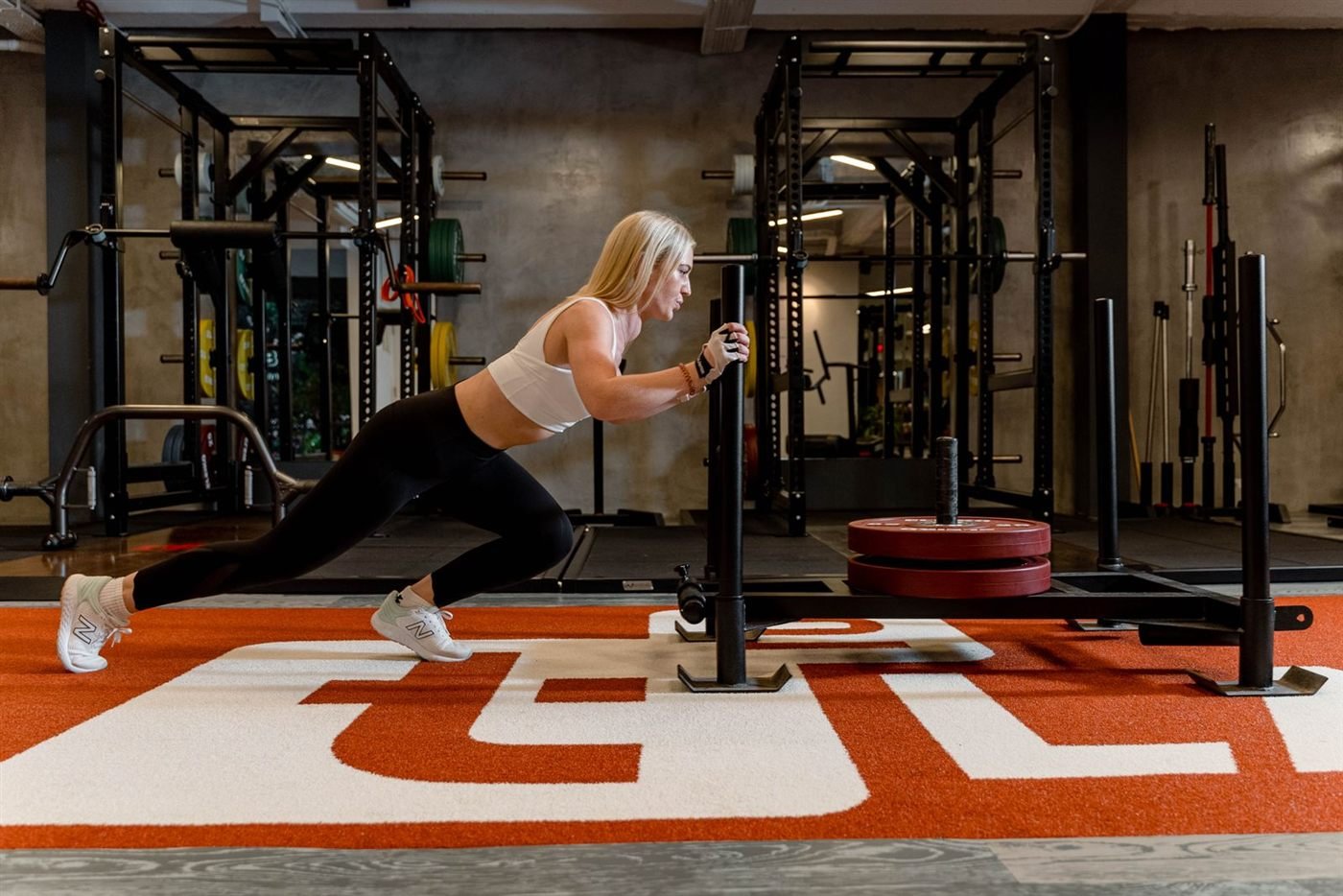 Mulher empurrando trenó (sled) durante treino funcional em academia