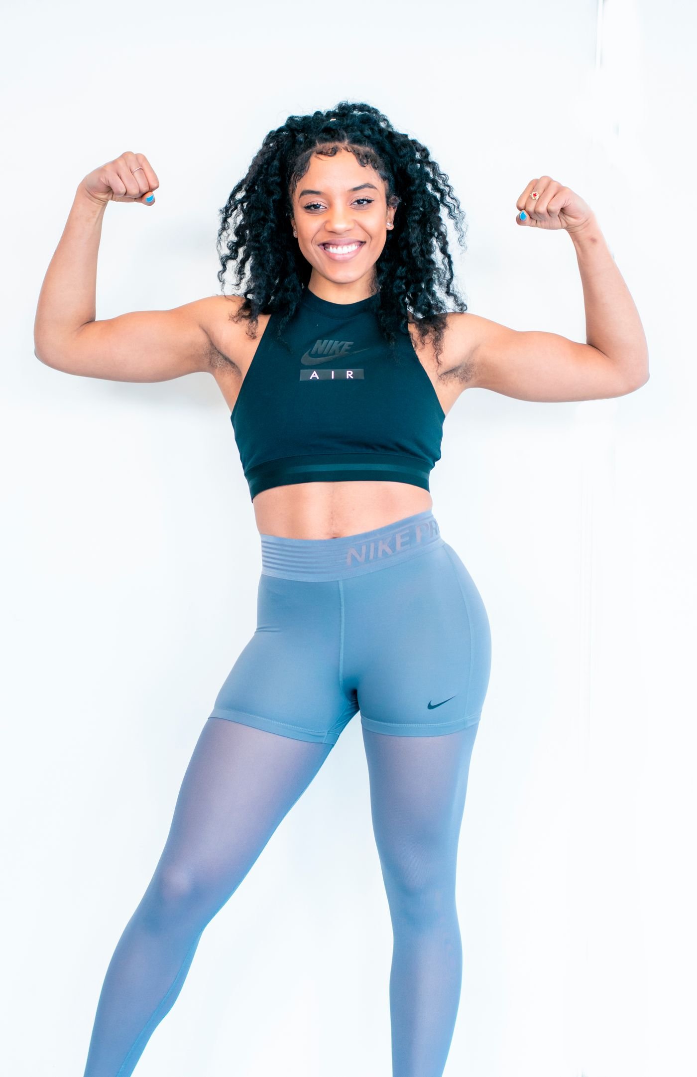 Mulher sorridente flexionando os bíceps para demonstrar força e definição muscular