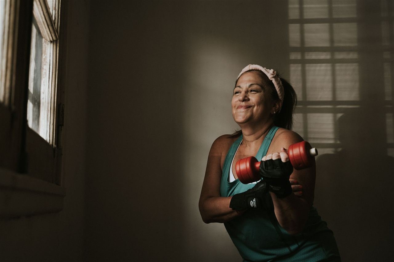 Mulher sorrindo durante exercício de rosca direta com halteres em treino de força