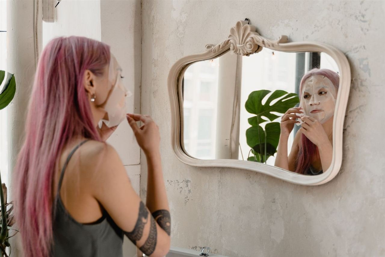 Mulher observando o próprio rosto no espelho durante cuidados com a pele