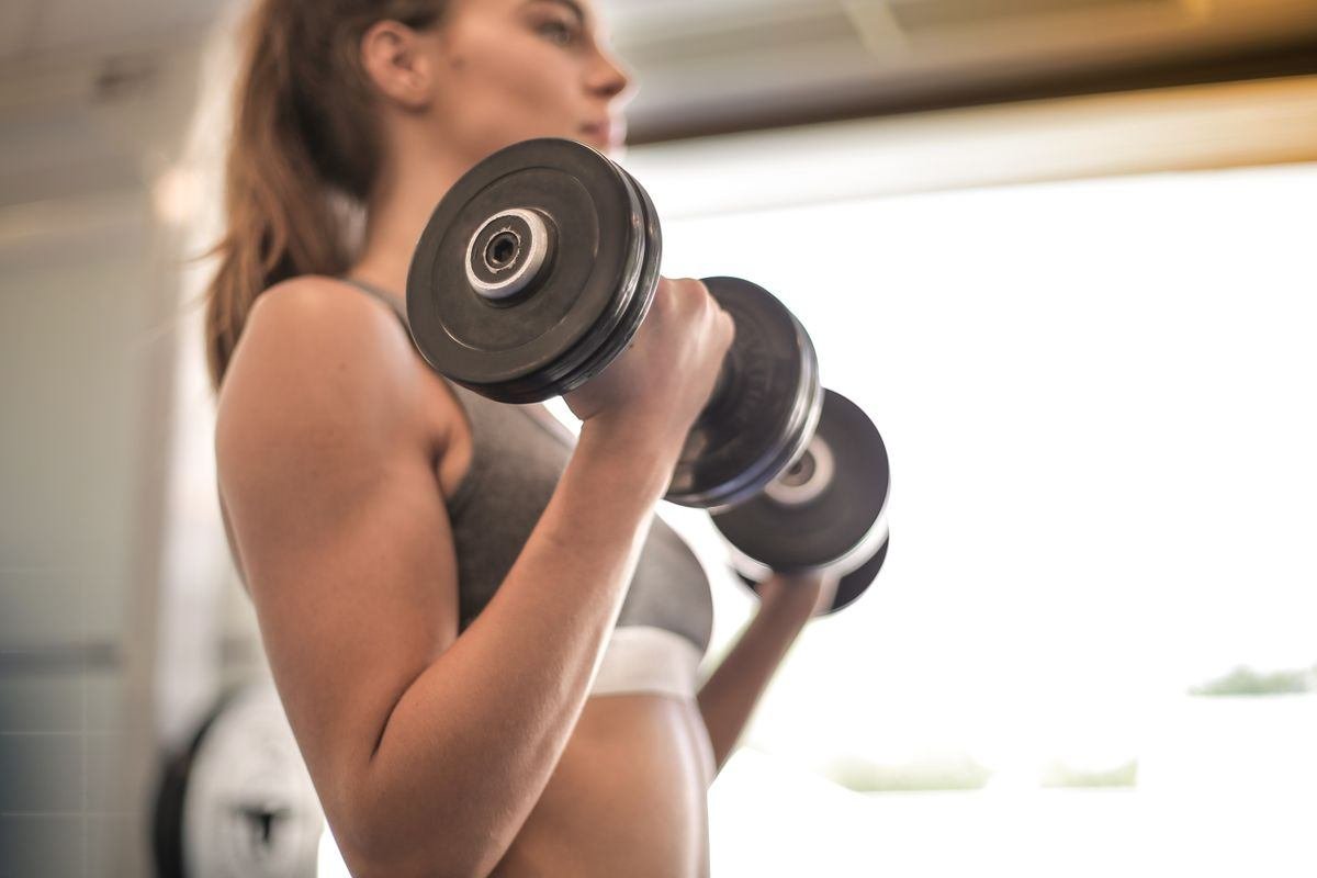 Mulher realizando rosca direta com halteres em treino de musculação