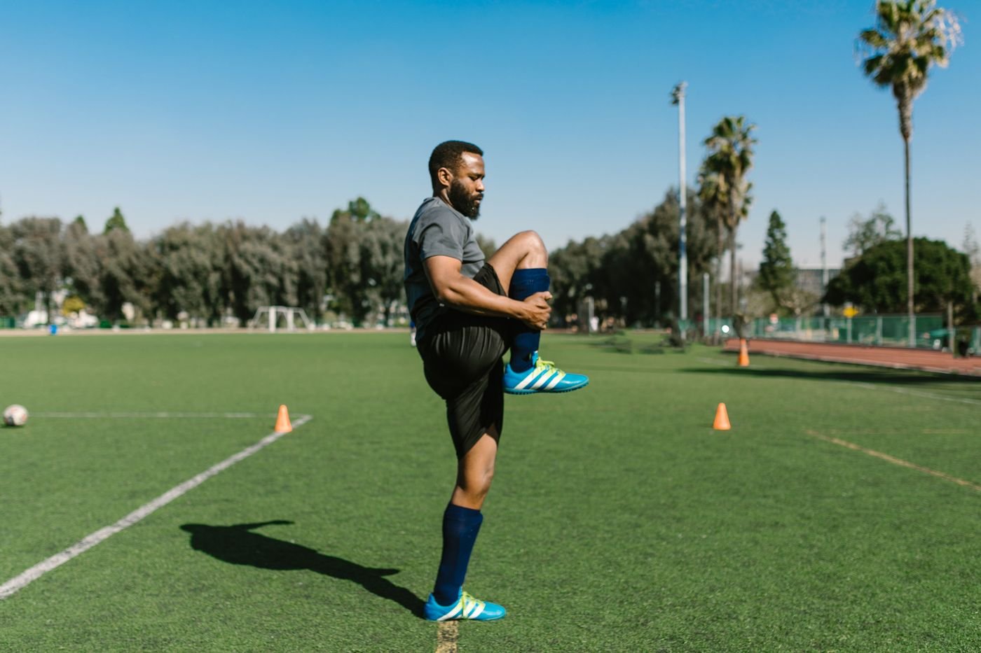 Homem alongando a perna em campo ao ar livre após o treino, aliviando a dor muscular