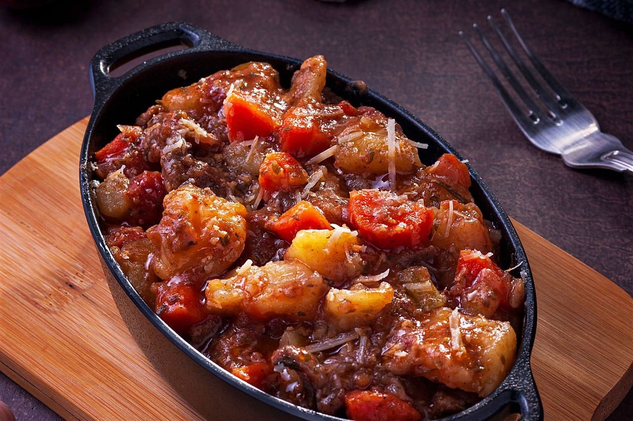 Picadinho de carne com legumes servido em panela de ferro sobre tábua de madeira
