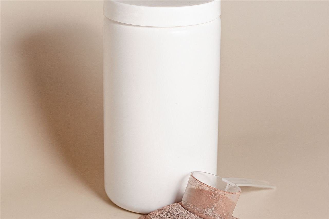 Pote de whey protein em pó com colher medidora ao lado