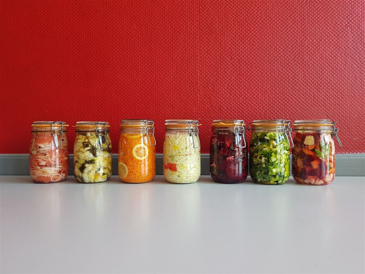 Fileira de potes de vidro com vegetais fermentados coloridos