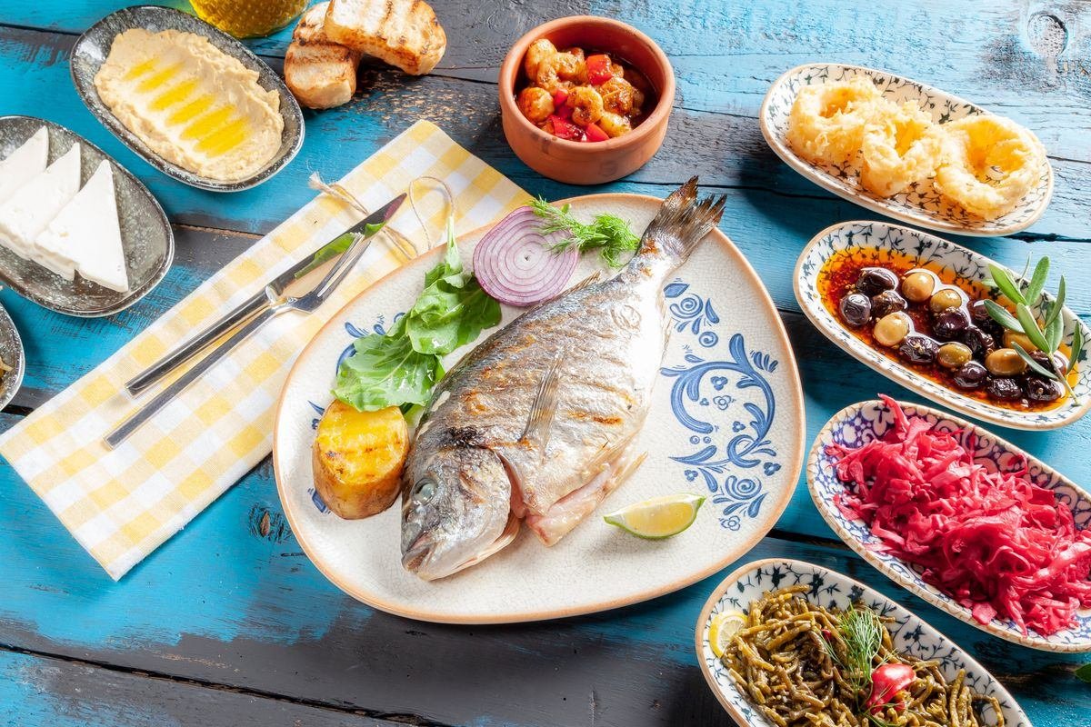 Mesa com peixe grelhado, azeitonas, queijos e vegetais no estilo da dieta mediterrânea