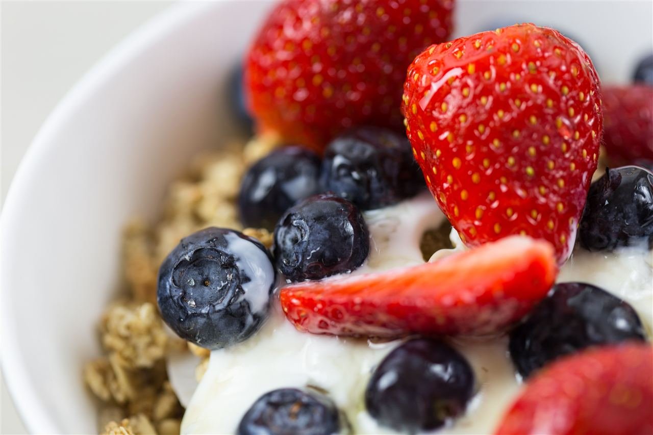 Tigela de iogurte grego com granola, morangos e mirtilos frescos
